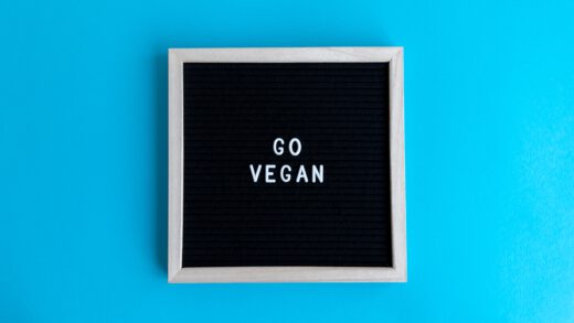 Czarna tabliczka z napisem "go vegan" w drewnianej ramce na niebieskim tle