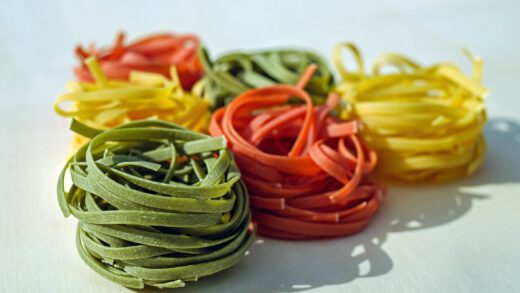 Kilka rodzajów kolorowego makaronu spagetthi zwiniętego w rolki i leżące obok siebie na białym tle
