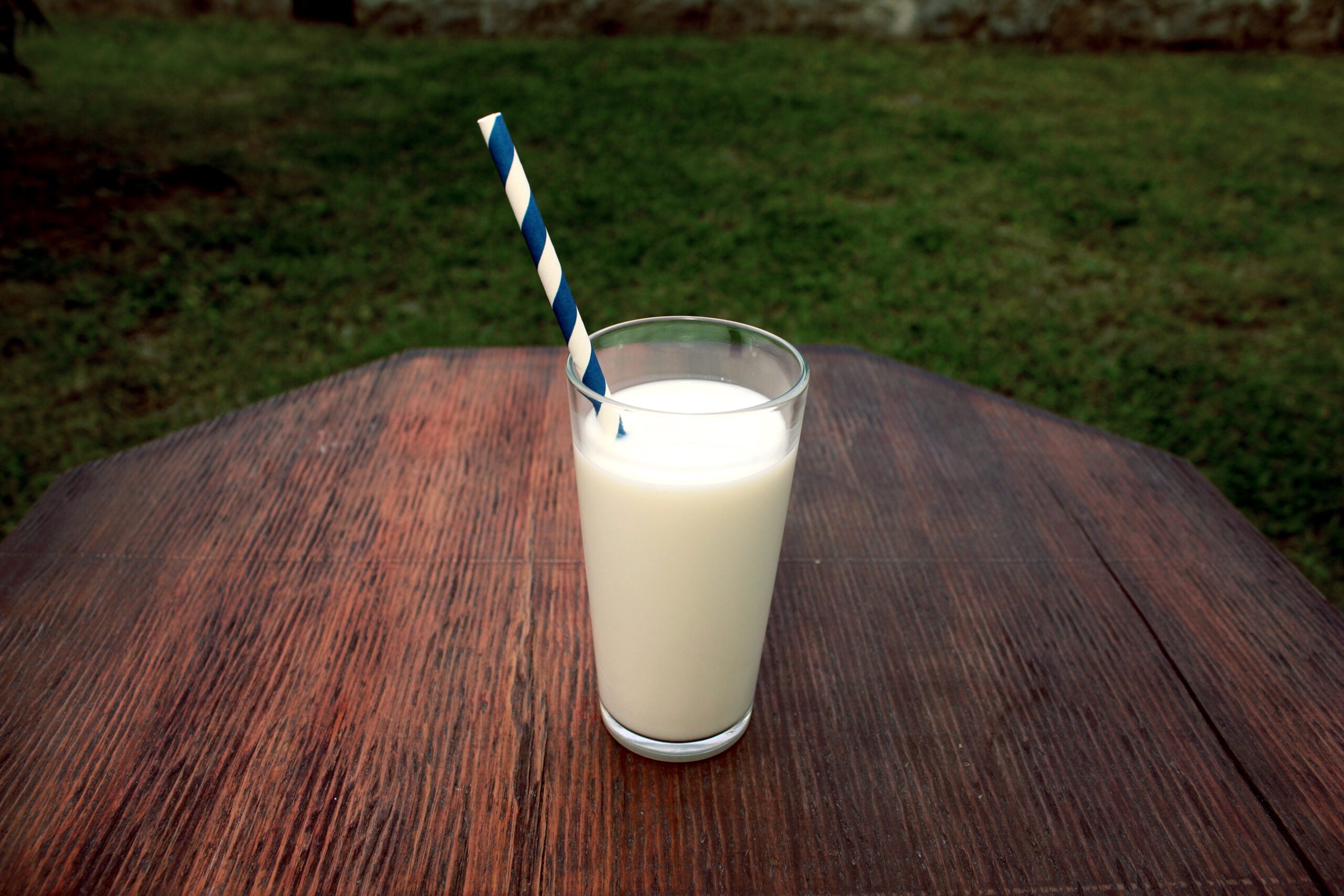 Szklanka mleka z papierową rurką do picia, stojąca na drewnianym stoliku na trawie w ogrodzie