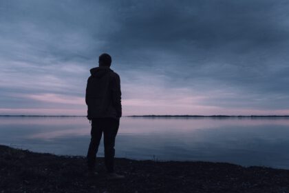 Widok od tyłu na mężczyznę stojącego nad jeziorem wieczorową porą