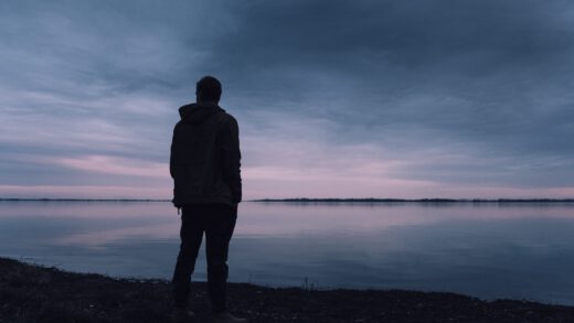 Widok od tyłu na mężczyznę stojącego nad jeziorem wieczorową porą