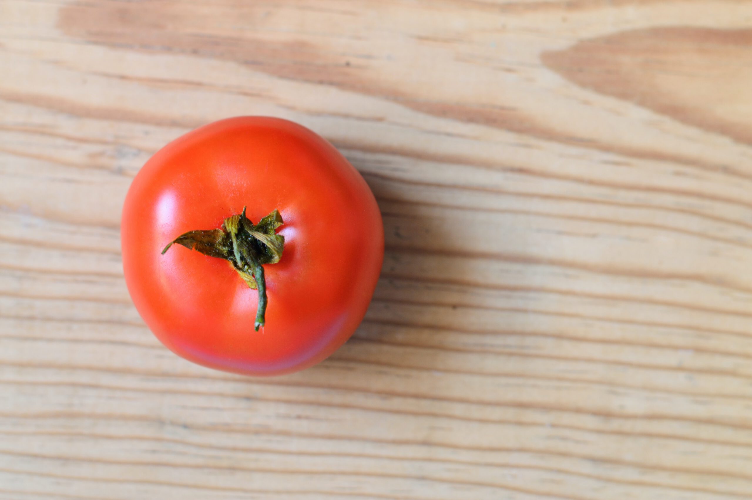 Widok z góry na czerwonego pomidora z zielonym ogonkiem, leżący na drewnianym blacie