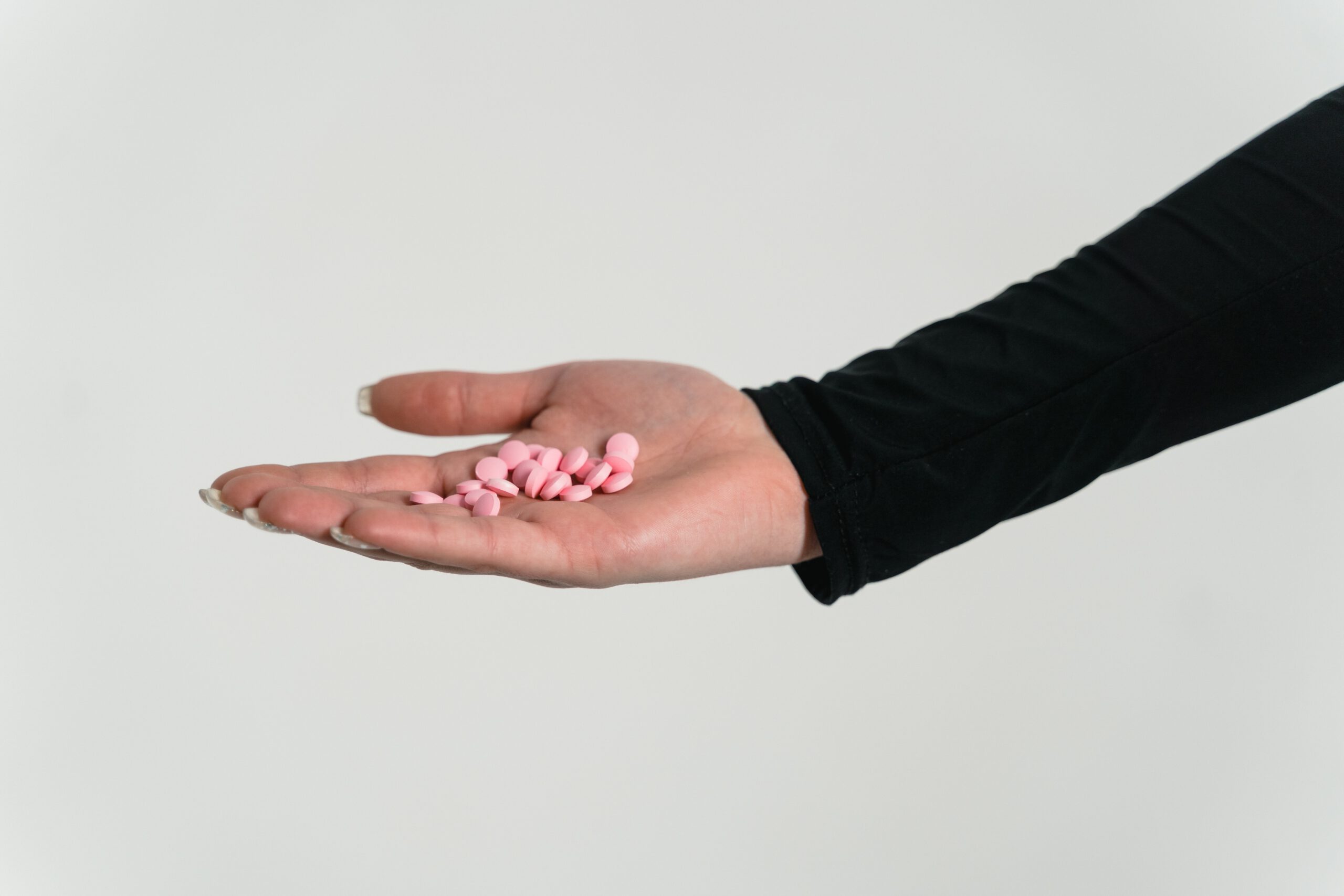 Wyciągnięta kobieca dłoń trzymająca witaminę A w postaci różowych tabletek