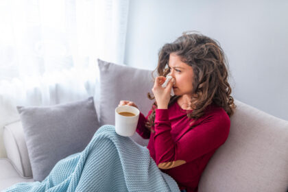 Kobieta podczas jesiennego przeziebienie siedzi na kanapie i pije gorącą herbate